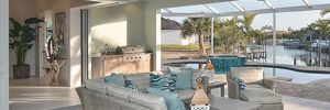 Covered patio with wicker furniture, ceiling fans, and outdoor kitchen, overlooking a pool and waterfront view.