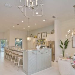 Open-concept kitchen and dining area with island seating, chandeliers, and pastel decor in a bright, modern home.