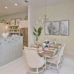 Modern kitchen and dining area with light-colored cabinets, a set table, wall art, and a large potted plant.