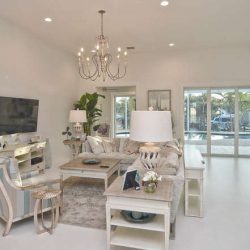 Modern living room with neutral decor, large windows, sectional sofa, chandelier, and view of a backyard pool.