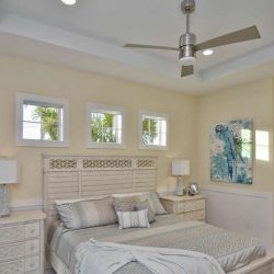 Neutral-toned bedroom with a ceiling fan, four small windows, and patterned bedding; tropical art on the wall.