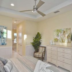 Bedroom with neutral walls, ceiling fan, dresser, chair, potted plant, and modern artwork on the walls.