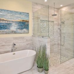 Modern bathroom with a freestanding tub, glass shower, two potted plants, and a seascape painting on the wall.