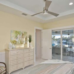 Bedroom with a ceiling fan, dresser, armchair, and sliding glass doors opening to a patio with a pool and outdoor seating.