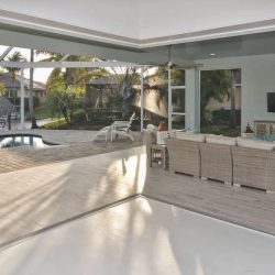 Modern living room with wicker furniture opens to a patio and pool area through large sliding glass doors.