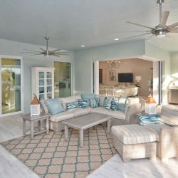 Spacious covered patio with wicker furniture, ceiling fans, outdoor kitchen, and sliding glass doors to indoor living area.