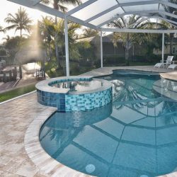 Screened-in backyard pool and spa area with tile accents, lounge chairs, and view of a canal with dock and palm trees.