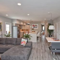 Modern open-plan living room and kitchen with gray sectional sofa, dining area, and colorful wall art.