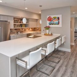 Modern kitchen with a large white island, four white bar stools, stainless steel appliances, and wall art.