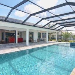 Enclosed outdoor swimming pool with patio seating and open access to a modern house under a clear sky.