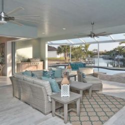 Covered patio with wicker furniture, decorative pillows, outdoor rug, ceiling fans, and view of a pool and waterfront.