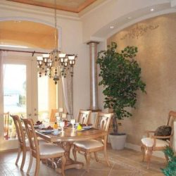 Dining room with wooden table and chairs, chandelier, large potted plant, and arched doorway with natural light.