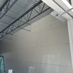 A partially finished drywall wall under a metal ceiling, with a green ladder and construction materials nearby.