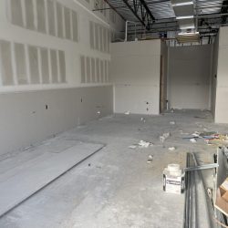 Unfinished interior space with exposed ceiling, drywall, scattered debris, and construction materials on the floor.
