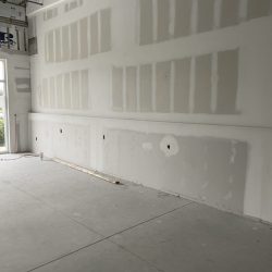 Unfinished interior wall with drywall installed, electrical outlets visible, and an exposed ceiling.