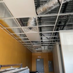 Ceiling under construction with exposed ducts, suspended ceiling grid, partially installed panels, and boxes below.