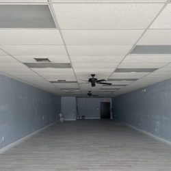 An empty, unfinished room with gray walls, tiled floor, ceiling fans, and an exit door at the back.