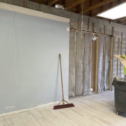 A person in a safety vest cleans debris near a wall under renovation with exposed insulation and studs.