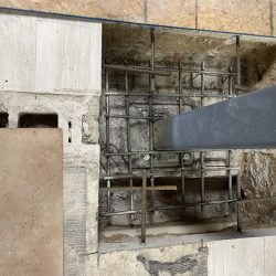 Exposed concrete floor section with steel reinforcement and a vertical steel column anchored in the center.
