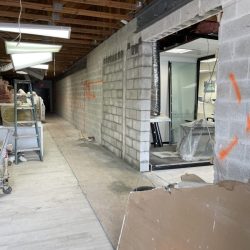 A hallway under construction with exposed ceiling beams, cinder block walls, and construction materials scattered around.