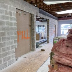 An interior under construction with exposed ceiling, pink insulation, and "FILL" spray-painted on a wall.