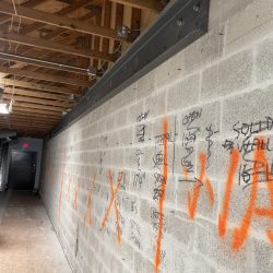 Concrete block wall with orange spray paint markings and black handwritten construction notes inside a building under renovation.