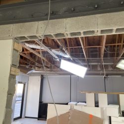 Exposed ceiling with wiring, ductwork, and lighting; partially demolished wall and construction debris below.